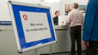 Menschen stehen in einem Arbeitsamt an einem Schalter in einer Warteschlange.