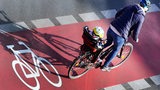 Eine Frau fährt mit ihrem Kind im Fahrradsitz über einen Radweg.