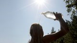Eine Frau schüttet sich im prallen Sonnenschein zur Erfrischung Wasser aus einer Flasche über den Kopf.