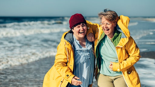 Serafia Johansson und Katharina Guleikoff mit gelben Regenmänteln, dahinter das Meer