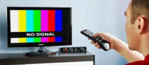 Ein Mann sitzt mit einer Fernbedienung vor dem Fernseher, auf dem "No Signal" steht (Symbolbild)