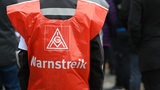 Ein Mensch trägt ein rotes Cape mit dem Logo der Gewerkschaft IG Metall, auf dem "Warnstreik" steht